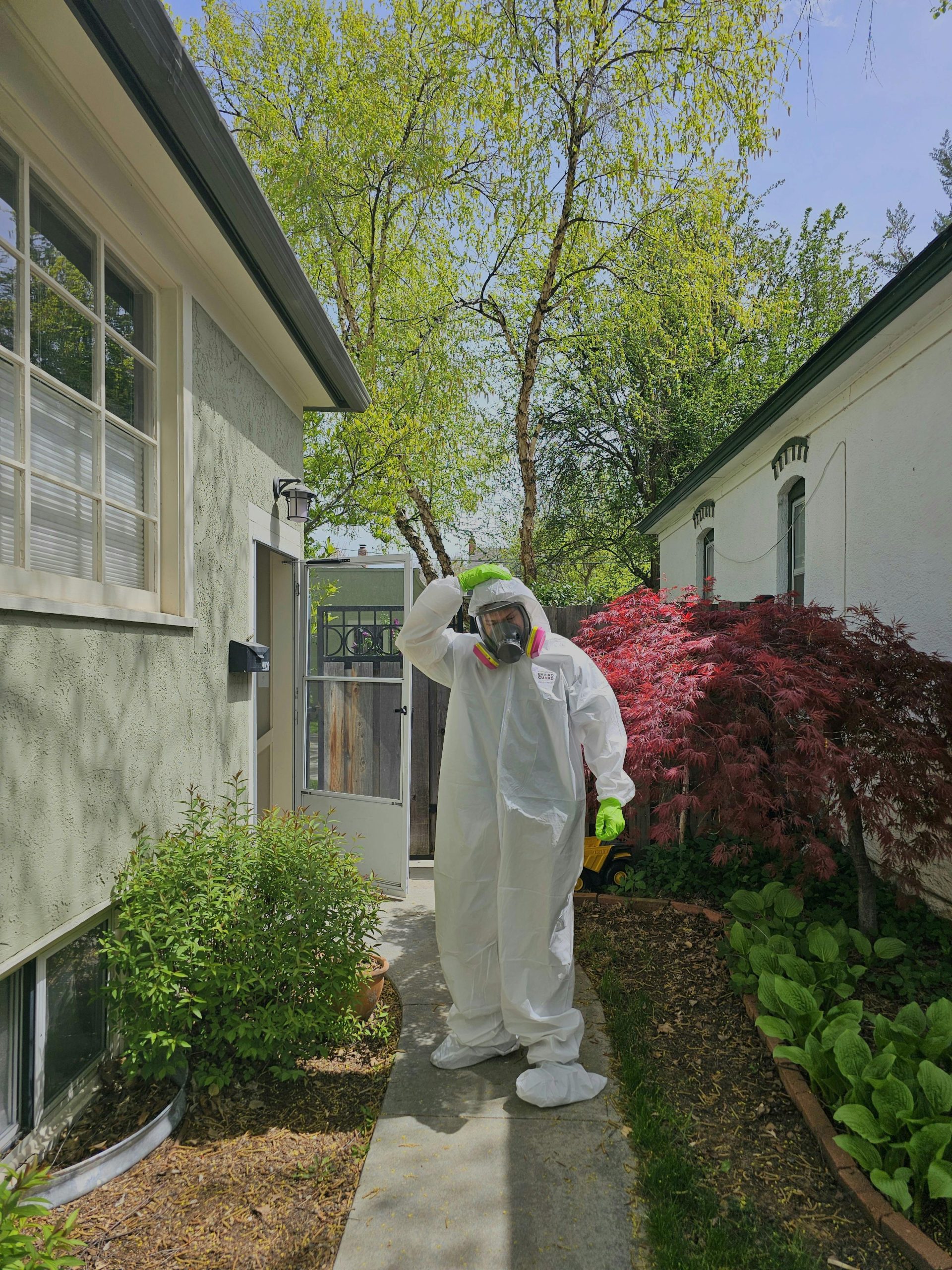 A person in protective gear and gas mask standing in a lush garden on a sunny day.