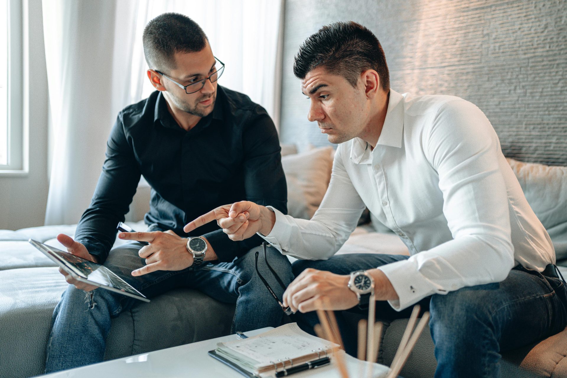 Two men in a home office discuss work on a tablet, highlighting teamwork and collaboration.